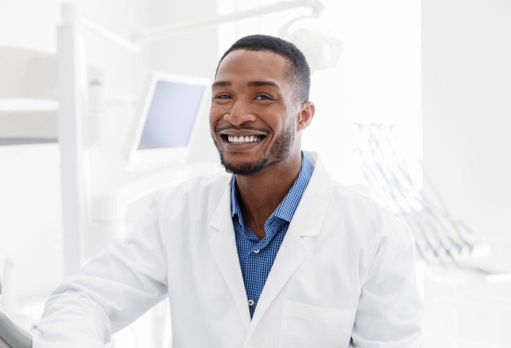 Handsome black dentist smiling over modern dental clinic background